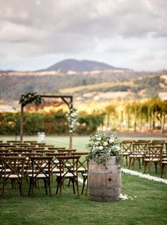 an outdoor ceremony setup with wooden barrels and flowers on the aisle, surrounded by chairs