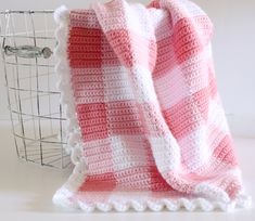 a pink and white blanket sitting on top of a table next to a wire basket