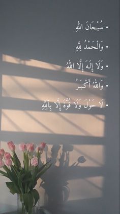 a vase filled with pink flowers sitting next to a window covered in arabic writing on a white wall