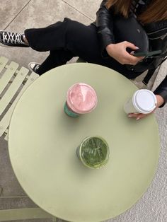 two people sitting at an outdoor table with drinks in their hands and one holding a cell phone