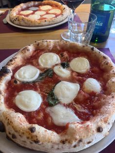 two pizzas sitting on top of a white plate next to glasses of water and wine