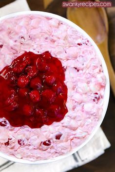 a white bowl filled with cranberry fluff and topped with cherries next to a wooden spoon