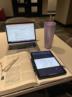 two laptops and a cell phone on a table with an open book next to it