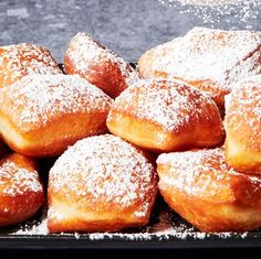 powdered sugar covered doughnuts are piled on top of each other in a black tray