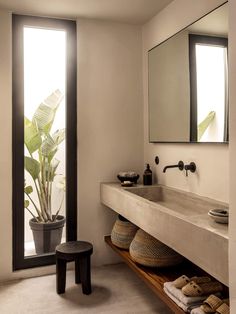 a bathroom with a sink, mirror and stool next to a plant in a pot