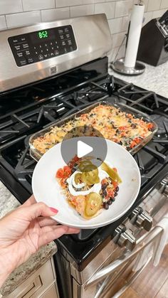 a person holding a plate with food on it in front of an oven and stove