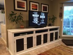 a flat screen tv sitting on top of a white entertainment center next to a window