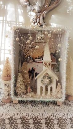 a small white church surrounded by christmas trees and other holiday decorations in a window frame