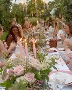 a group of people sitting around a table with plates and candles in the middle of it