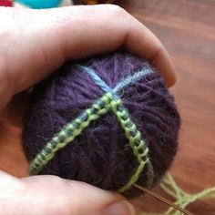 a hand holding a ball of yarn with needles in the foreground and knitting needles in the background