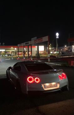 a white sports car parked in front of a gas station at night with its lights on