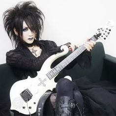 a woman sitting on a couch with a guitar in her hand and makeup painted black