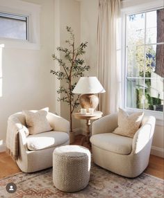 a living room with two chairs and a table in front of a large window that has a lamp on it