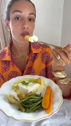 a woman sitting at a table eating food from a plate with carrots and green beans