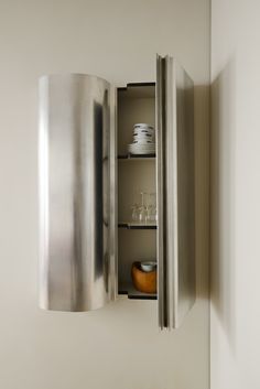 a stainless steel wall mounted cabinet with wine glasses and plates in the bottom shelf, next to a white wall