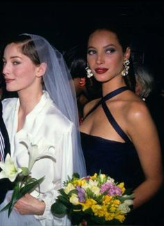 two beautiful women standing next to each other in front of a man wearing a suit and tie