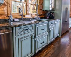 a kitchen with green cabinets and stainless steel appliances, along with wood flooring that matches the walls