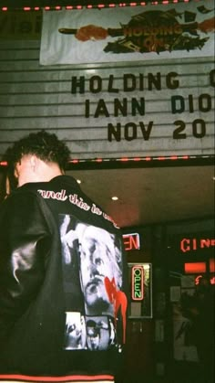 a man standing in front of a movie theater wearing a jacket with pictures on it