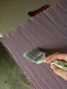 a person is using a brush to paint a rug on the floor with purple yarn