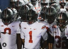 a group of football players standing next to each other wearing helmets with numbers on them