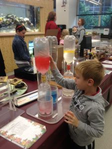 a young boy is pouring liquid into a beakle at a science fair with other people in the background