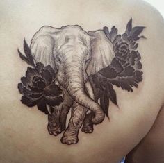 an elephant and flowers tattoo on the back of a woman's shoulder, which is covered in black ink