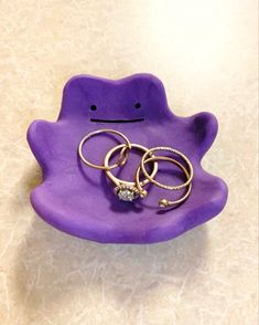 two rings are sitting on top of a purple frog shaped tray that has been placed on the floor