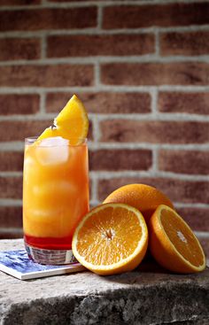 an orange drink sitting on top of a table next to sliced oranges and a brick wall