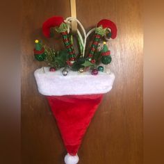 a red and white christmas hat hanging on a door with green plants in it's corner