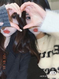 two girls are holding their hands up to their faces and making the shape of a heart