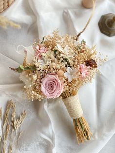 a bridal bouquet with dried flowers on a white table cloth next to other items