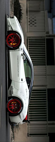 the rear end of a white sports car parked on the side of a road next to a tall building