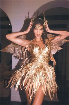 a woman in a gold costume with feathers on her head and hands behind her head