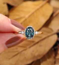 a woman's hand holding an engagement ring with a blue diamond in it and leaves behind her