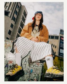 a woman sitting on top of a piece of luggage in front of some tall buildings