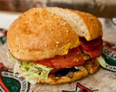 a sandwich with meat, lettuce and tomato on it sitting on a wrapper