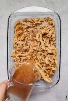 a person is holding a glass in front of a dish with some food on it