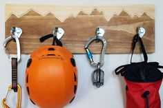 Handmade wall hanger, using rock climbing hangers mounted to a sanded pine board. The mountains are cut into the board and stained. Picture hangers included on back, ready to be mounted on the wall. (Please do not attempt to climb, picture hangers are not rated for human loads.) The 4 hanger board is 22 x 7.25 x .75 The 3 hanger board is 16 x 7.25 x .75 The 2 hanger board is 12 x 7.25 x .75 Climbing Gear Storage, Climbing Gear Organization, Outdoor Gear Storage, Mountain Board, Rock Climbing Gifts, Kayak Storage Rack, Gear Room, Climbing Gifts, Gear Storage