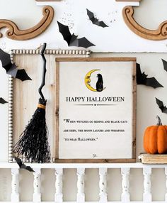 a happy halloween sign with bats hanging from it's sides and a black cat sitting on top