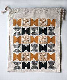 an orange, black and white geometric design on a linen bag with tassels