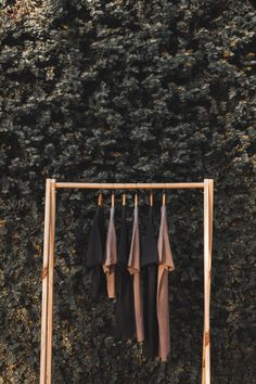 four shirts hanging on a clothes rack in front of a wall covered with ivy leaves