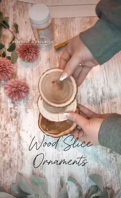 two hands are holding a wooden slice ornament on top of a table with flowers