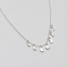 "The Moon Phases Necklace is a chic, stylish piece that can be worn with almost anything! The 7 various moon pendants dangle lightly from a delicate 16\" cable chain that features a 2\" extender (max necklace length is 18\"). - Available in 14K Gold Plated Brass or Rhodium Plated Sterling Silver - Handmade - FREE SHIPPING within the United States" Silver Dangle Charm Necklace With Moon Charm, Minimalist Moon Shape Charm Necklace With Clavicle Chain, Minimalist Silver Necklaces With Dangling Charms, Minimalist Silver Necklace With Dangling Charms, Adjustable Moon Phase Charm Necklace, Minimalist Moon Phase Charm Necklace, Dainty Half Moon Charm Necklace With Moon Phase, Delicate Moon Phase Charm Necklace, Dainty Half Moon Phase Charm Necklace