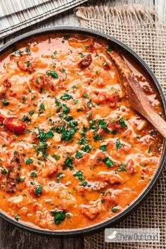 a skillet filled with meat and vegetables on top of a wooden table next to a spoon