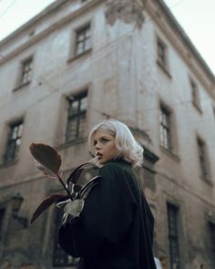 a woman standing in front of an old building holding a flower and looking at the camera