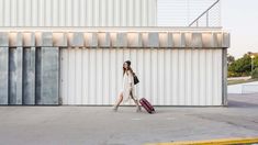 a woman is walking with her luggage in front of a white building that has vertical striped walls