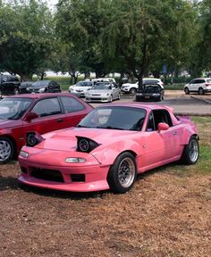 two pink cars parked next to each other in a parking lot with trees and grass