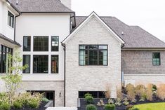 a large white brick house with lots of windows and plants in the front garden area