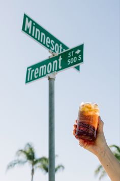 a person holding up a drink in front of a street sign that reads minnesota and tremont