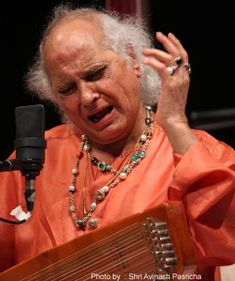 an older woman holding a musical instrument in front of a microphone with her hands up